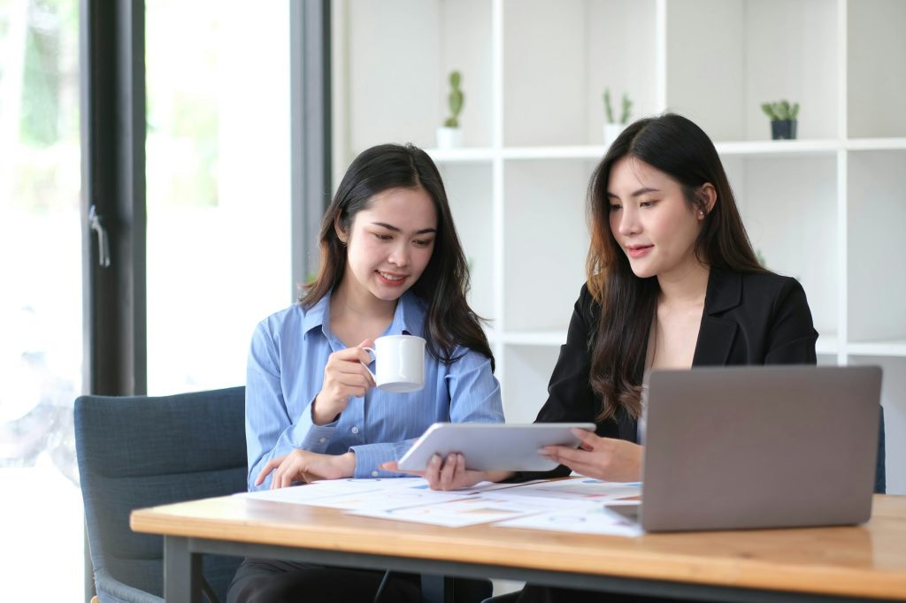 Two young Asian businesswoman discuss investment project working and planning strategy.